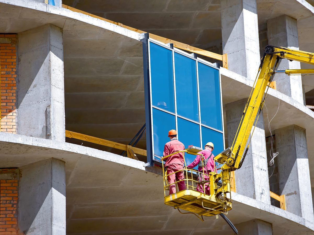 Arbeiter im Hebekorb installieren Glaspaneele einer Vorhangfassade